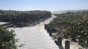A wooden boardwalk leading to a beach with dense vegetation on both sides.