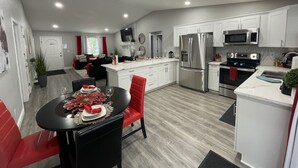 A modern kitchen with white cabinets, stainless steel appliances, and a dining area with red chairs and a black table.