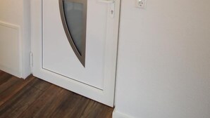 Eine weiße Tür mit einer satinierten Glasscheibe, ein runder Spiegel an der Wand und eine schwarze Fußmatte vor der Tür.