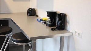 Eine moderne Küche mit weißer Arbeitsplatte, schwarzen Barhocker, einer Kaffeemaschine und einer Wanddekoration mit einem Blatt.