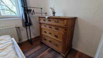 Eine Holzkommode mit vier Schubladen, ein Heizkörper, ein Fenster mit Vorhängen und eine Pflanze auf der Kommode.