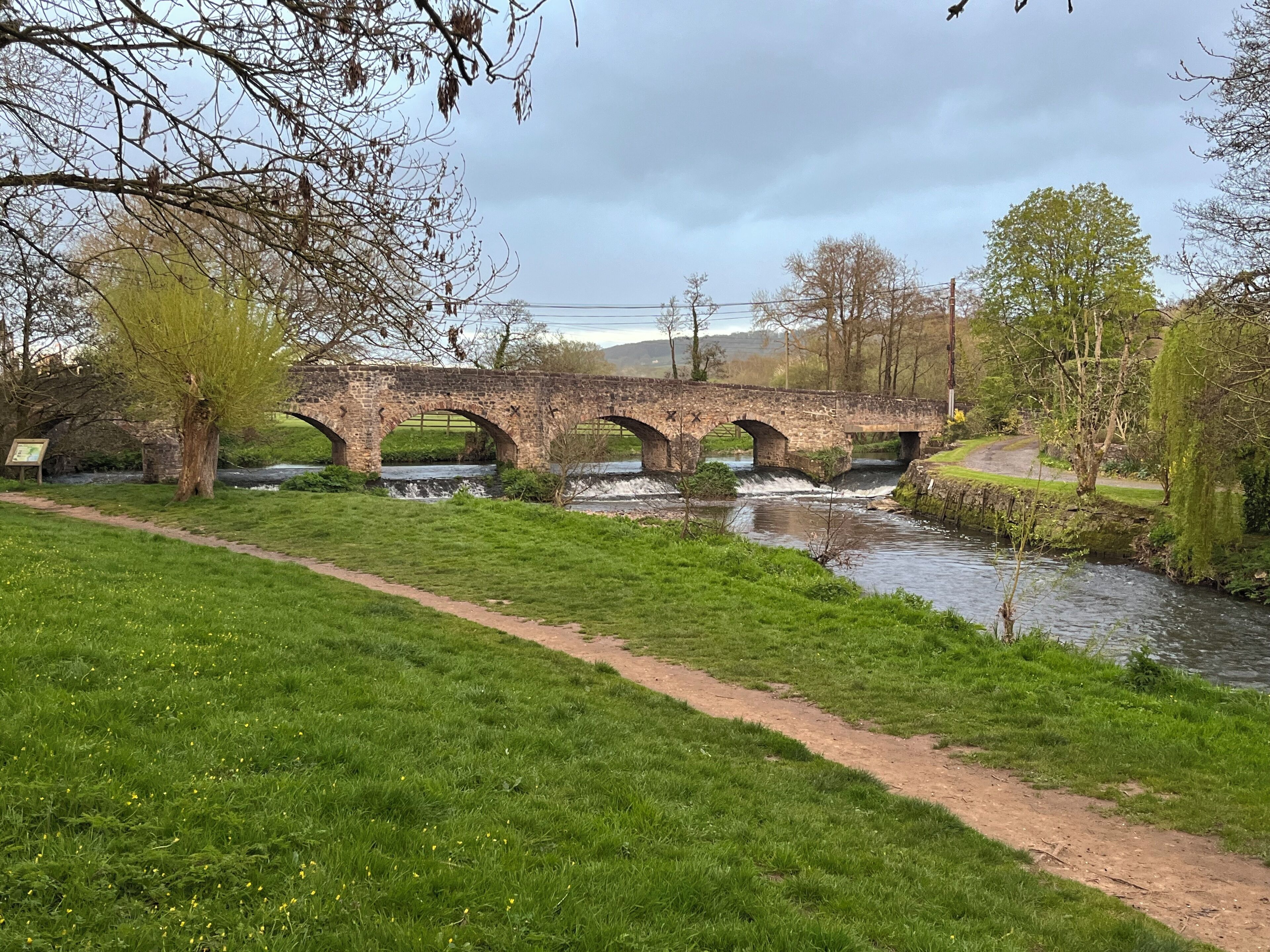A stone bridge over a river with a grassy path beside it.