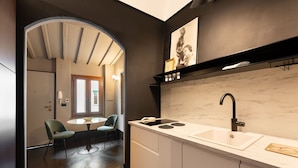 A modern kitchen with a white countertop, black faucet, and a marble backsplash. There is a dining area with a round table and chairs visible through an archway. - New Listing: Oltrarno Nest with Court, San Frediano area (Firenze)