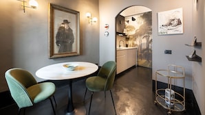 A modern interior with a round table, two green chairs, a framed picture, wall-mounted lights, and a small kitchen area. - New Listing: Oltrarno Nest with Court, San Frediano area (Firenze)