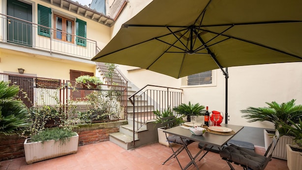 A patio area with a table, chairs, and an umbrella. There are potted plants and a staircase leading to an upper floor. - New Listing: Oltrarno Nest with Court, San Frediano area (Firenze)