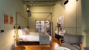 A bedroom with a four-poster bed, a small round table, a patterned armchair, and a wall-mounted lamp. - New Listing: Oltrarno Nest with Court, San Frediano area (Firenze)
