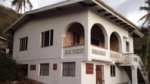 A two-story building with a white facade, multiple windows, and a stone accent wall. - Spacious 2-bed House in Carriacou (Hillsborough)
