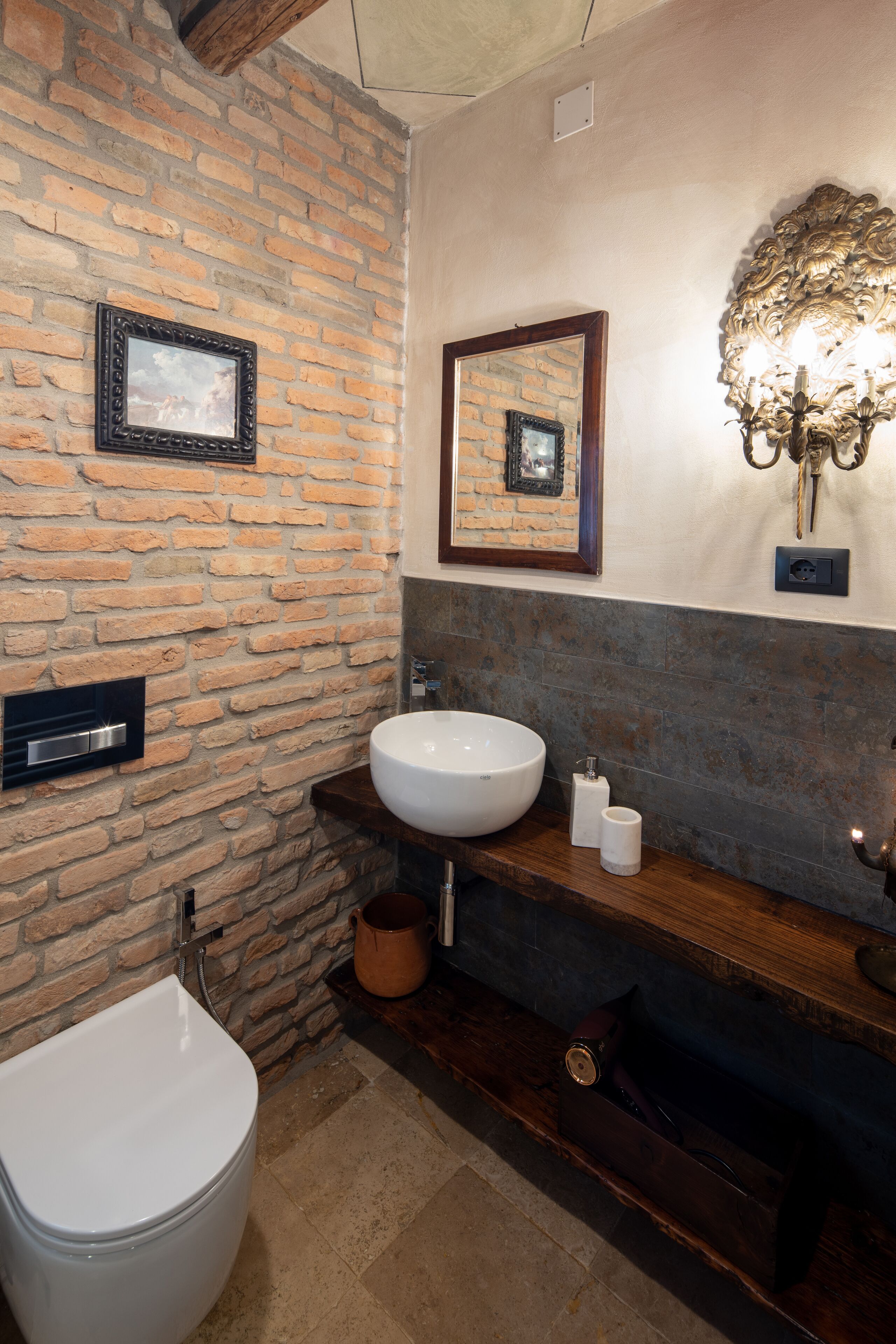 A bathroom with a stone wall, a white sink, a mirror, and a wooden vanity.