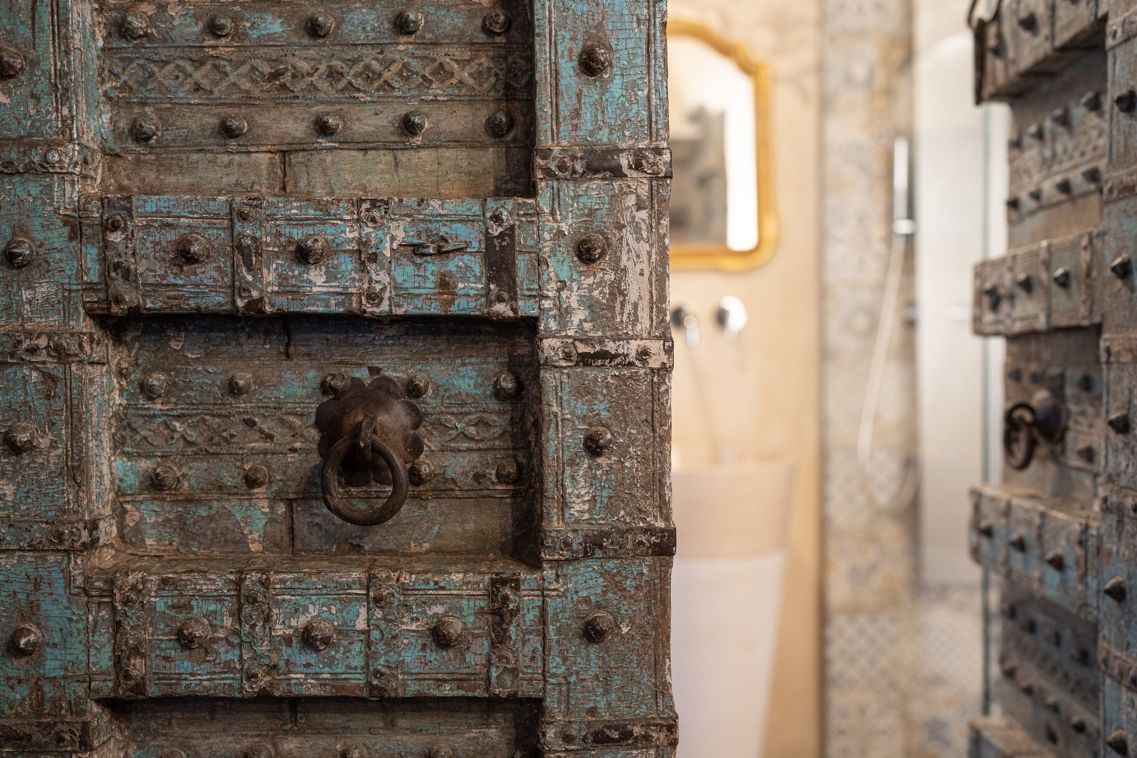 Un primer plano de una puerta rústica y desgastada con un picaporte de metal, rodeada de puertas similares con superficie texturizada y remaches.