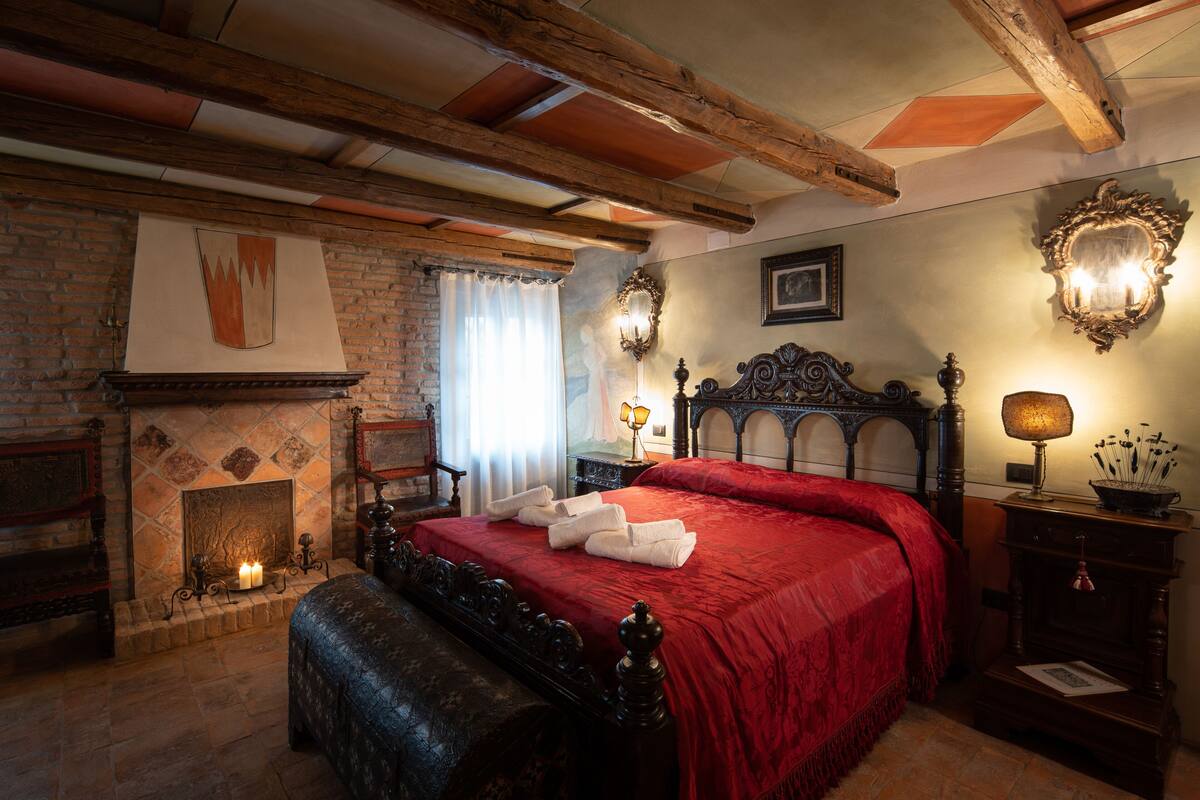 Una habitación tradicional con chimenea, una cama con ropa de cama roja y techo de madera.