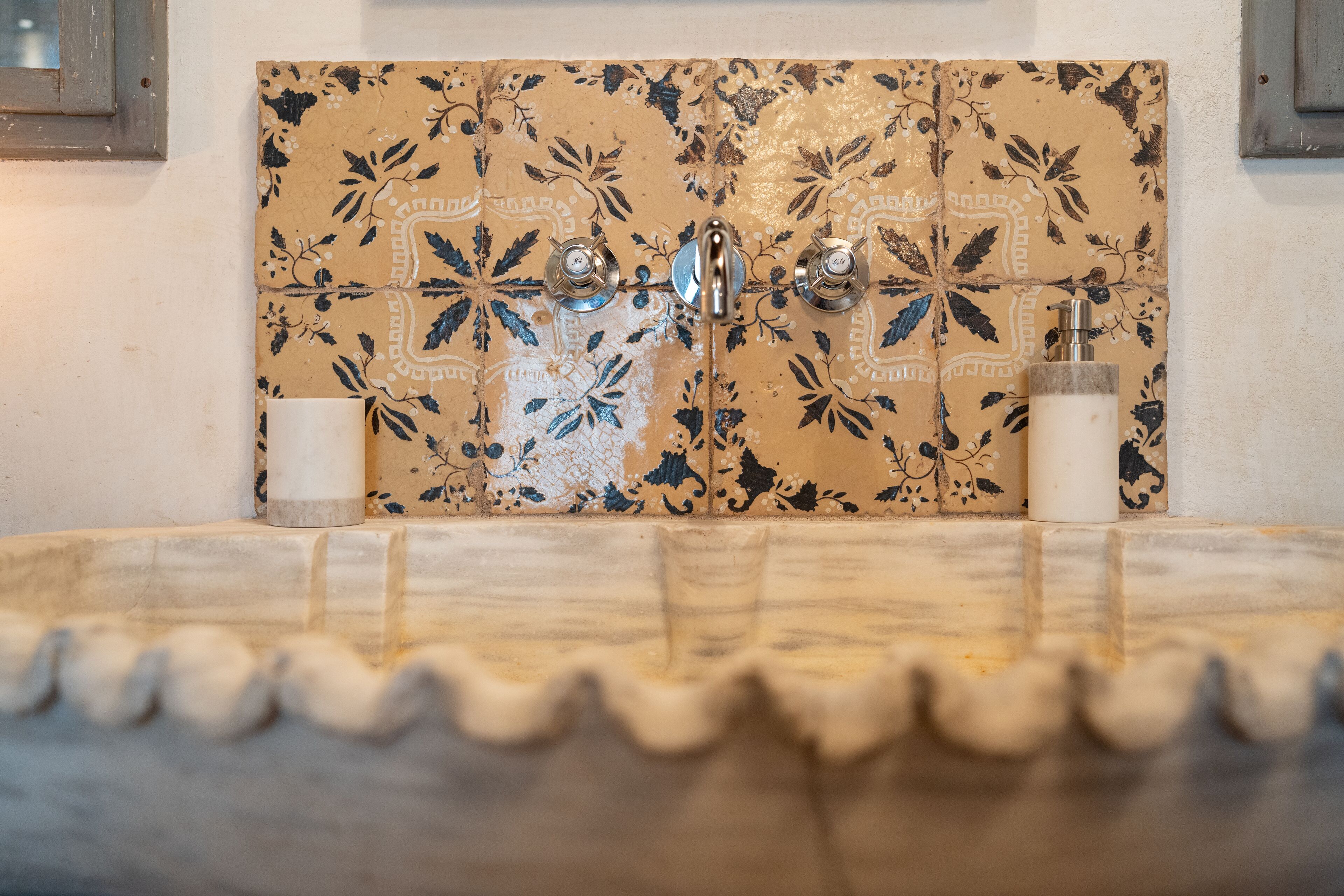 Un baño con pared de azulejos, un lavabo y una botella de jabón para manos.