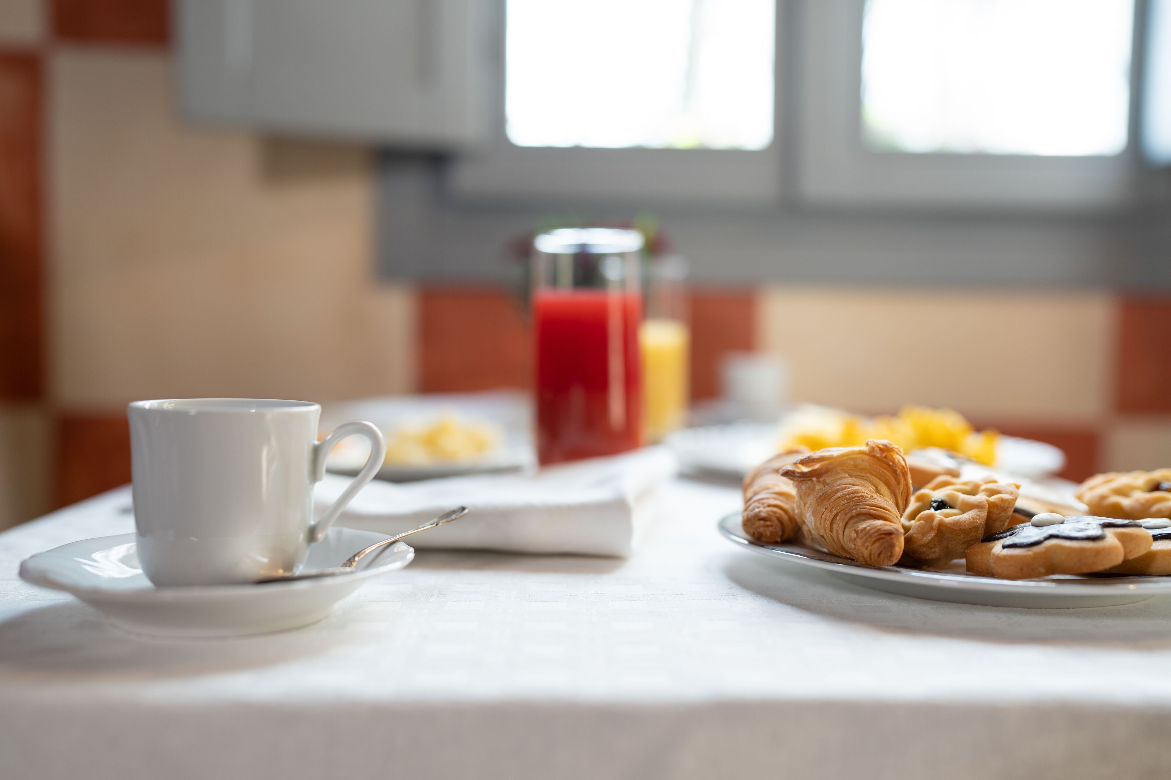Una mesa de desayuno con una taza, un vaso de jugo rojo y bollería.