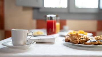 Una mesa de desayuno con una taza, un vaso de jugo rojo y bollería.