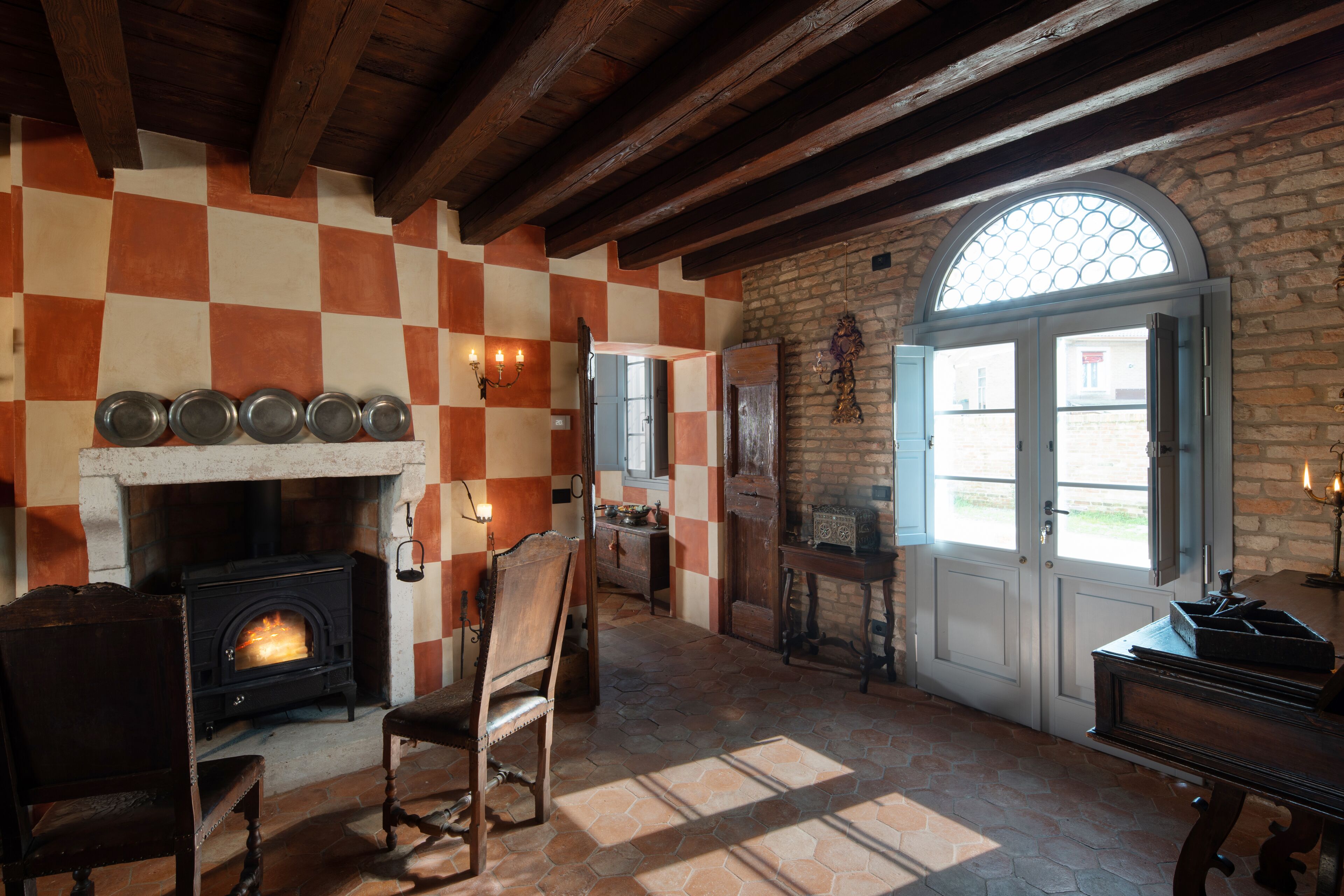 A rustic room with a fireplace, checkered walls, and a large arched window.
