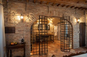 Una habitación rústica con paredes de ladrillo visto, una mesa de madera con fruta y una botella, y una reja de metal.