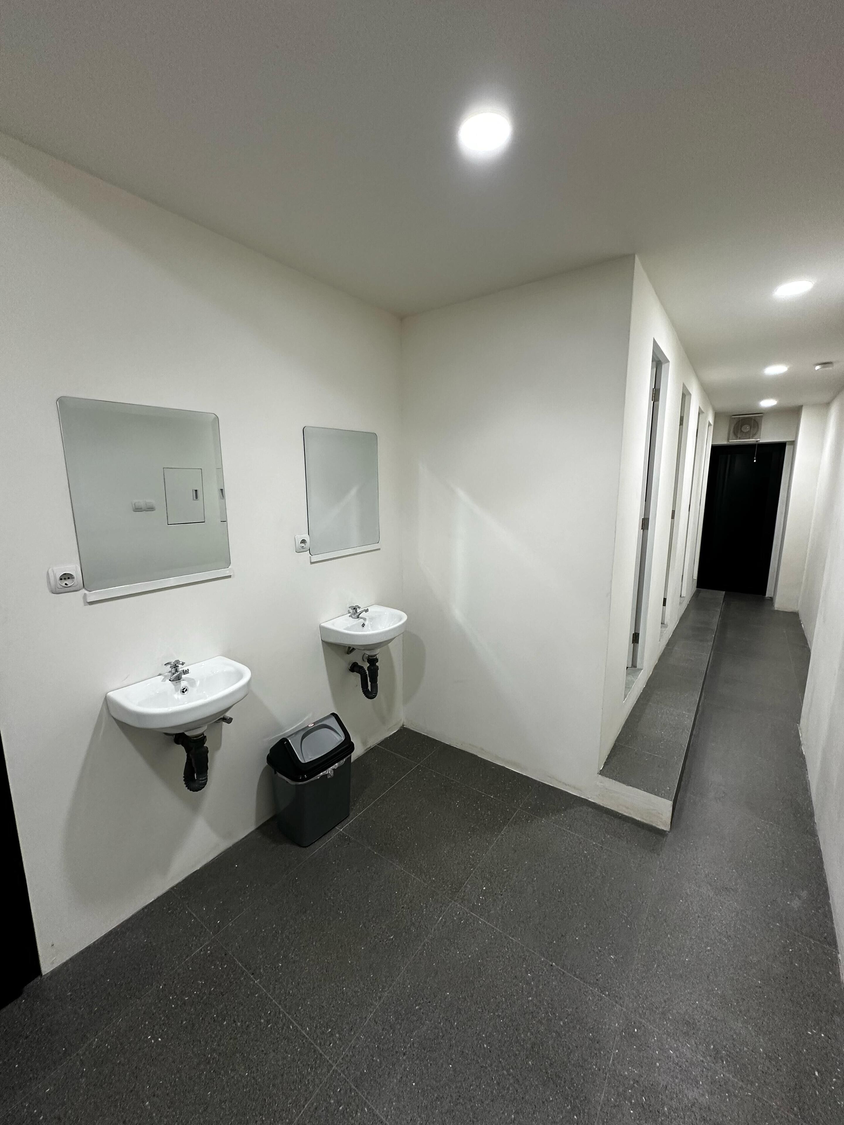 A corridor with two sinks, a trash bin, and a mirror on the wall.