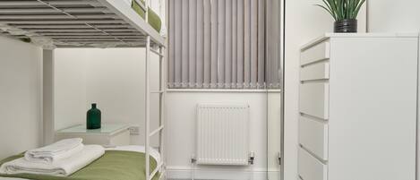 Una cama litera con un edredón verde, un radiador, una planta en maceta y un armario blanco.