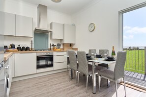 A modern kitchen with white cabinets, a built-in oven, and a dining area with grey chairs and a glass table.