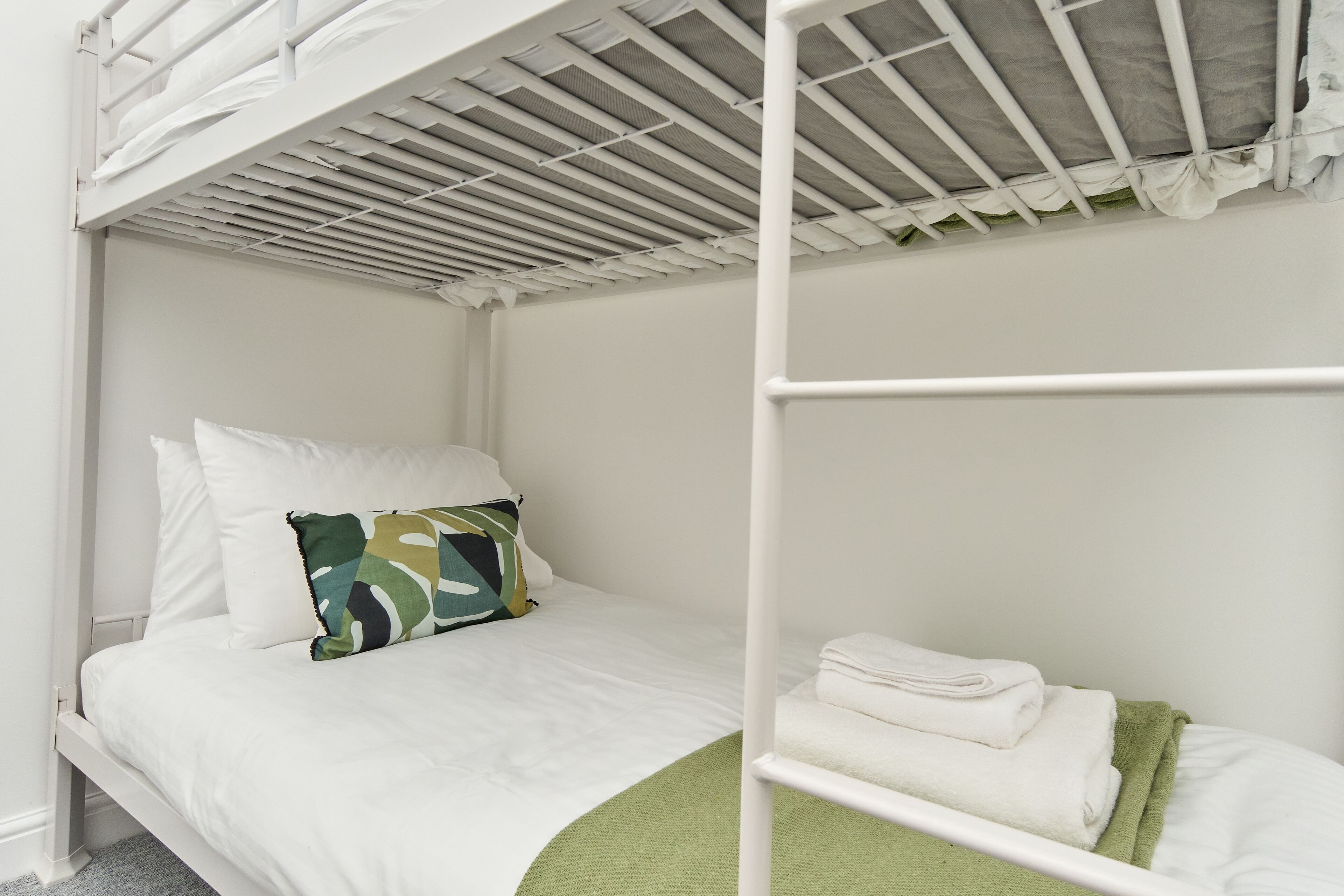 Un lit superposé avec une literie blanche et un plaid vert.