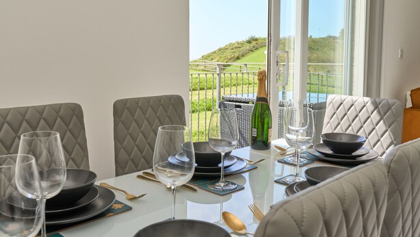 A dining table set with plates, bowls, and wine glasses, overlooking a grassy landscape. - The Penthouse In Bonchurch  (Ventnor)