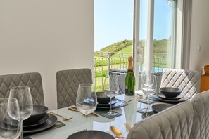 A dining table set with plates, bowls, and wine glasses, overlooking a grassy landscape. - The Penthouse In Bonchurch  (Ventnor)