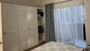 Ein Schlafzimmer mit einem Bett, einem Kleiderschrank, einem Deckenventilator und einem Fenster mit Vorhängen.