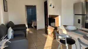 Ein modernes Wohnzimmer mit einer Couch, einem Essbereich mit Tisch und Stühlen, einer Küche mit Kühlschrank und einem Deckenventilator.