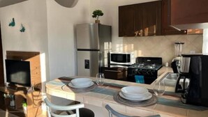 Eine moderne Küche mit Essbereich, ausgestattet mit Kühlschrank, Mikrowelle, Herd und einem kleinen Esstisch mit Stühlen.