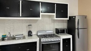 A kitchen with black cabinets, a stainless steel stove, a microwave, and a refrigerator. - Oasis Apartment (Puerto Vallarta)