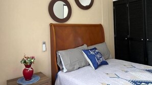 A bedroom with a wooden headboard, two round mirrors, a bed with a patterned bedspread, a red vase with flowers, and a black wardrobe. - Oasis Apartment (Puerto Vallarta)
