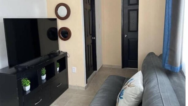 A living room with a TV on a black stand, a grey sofa, and three wall-mounted circular mirrors. - Oasis Apartment (Puerto Vallarta)