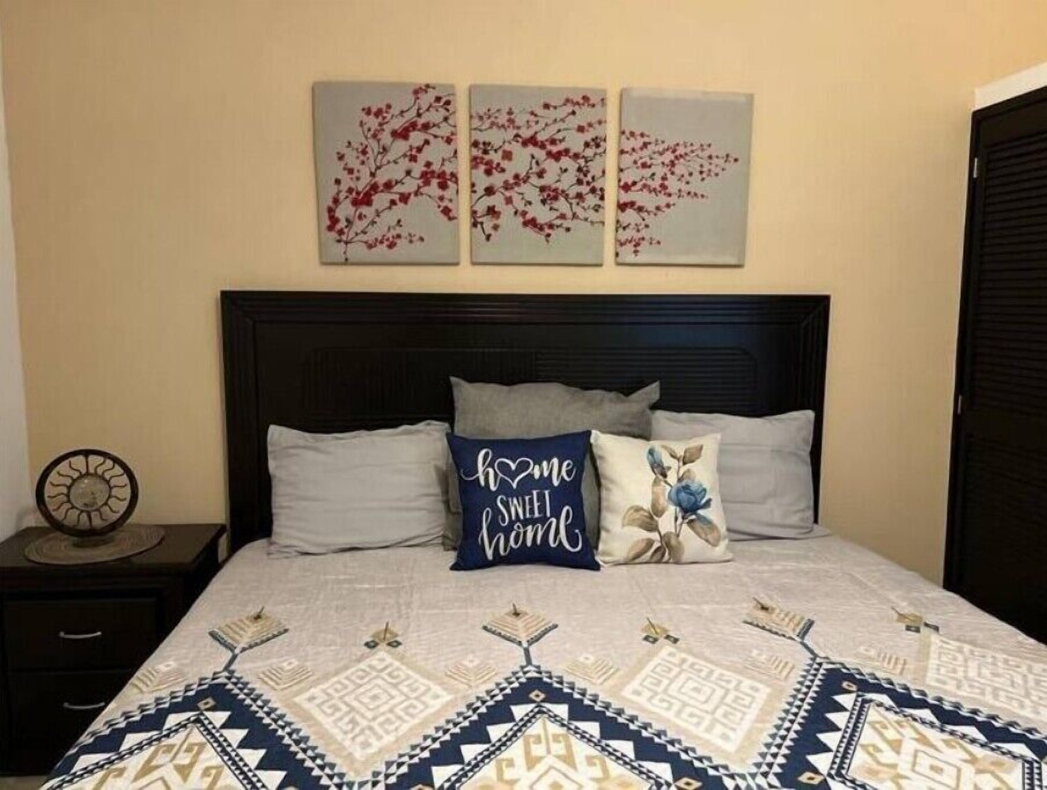 A neatly made bed with a patterned bedspread, a dark headboard, and three wall-mounted floral paintings.