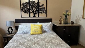 Une chambre à coucher comprenant un lit, une table de chevet, une lampe, une commode et une œuvre d’art murale.