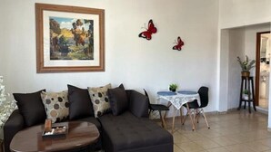 Un salon avec un canapé foncé, une table basse, un tableau encadré, deux décorations murales en forme de papillons rouges et une petite table ronde avec des chaises.