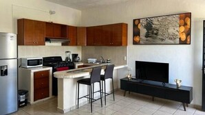 Une cuisine moderne avec des armoires en bois, un îlot central intégré, un four à micro-ondes, une cuisinière et un meuble TV noir.
