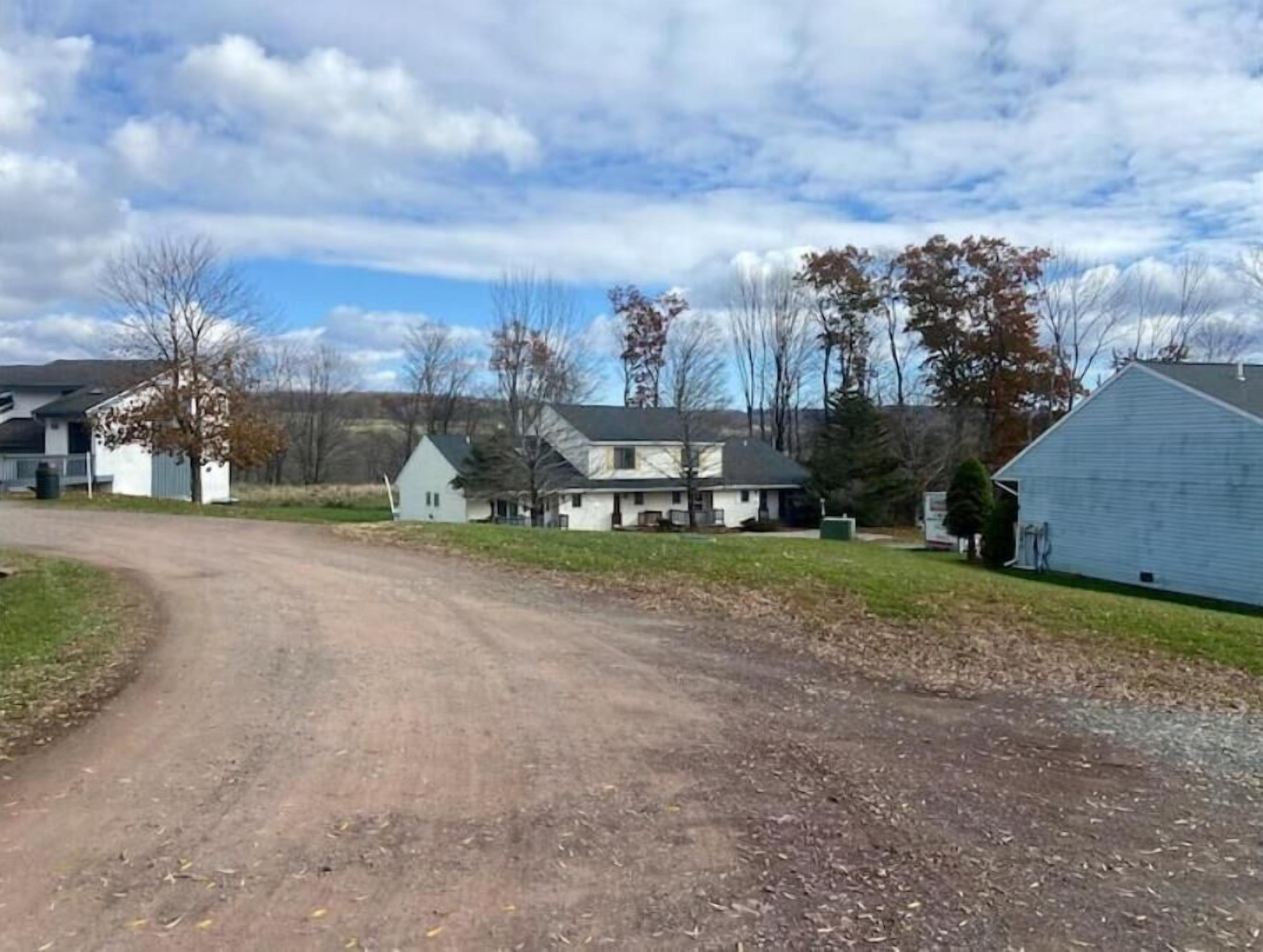 Une route de campagne qui mène à un groupe de maisons, avec un ciel dégagé au-dessus.