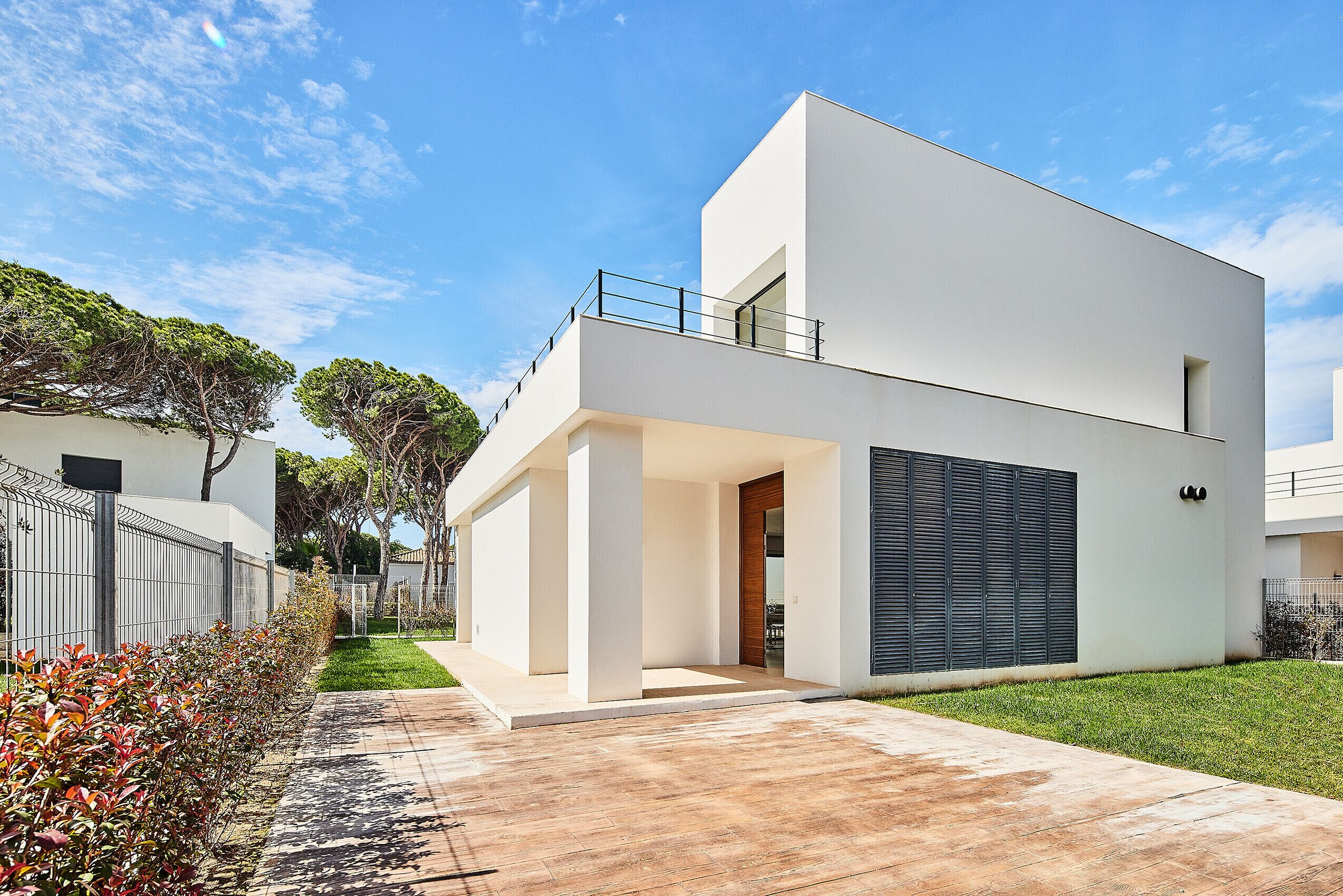 Een modern huis met twee verdiepingen, een plat dak, een balkon en een groot raam.