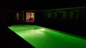 Een zwembad met een groen licht, een deur die leidt naar een ruimte met een tafel en stoelen, en een raam met gordijnen.
