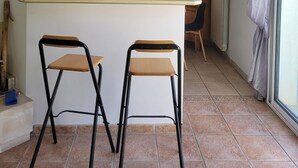 Een keuken met een centraal kookeiland, twee barkrukken, een magnetron, een koelkast en een kast met glazen deuren.