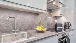 A modern kitchen with a stainless steel sink, a bowl of fruit, a kettle, and a toaster. - Central Windsor 1BR | Steps from Attractions (Windsor)