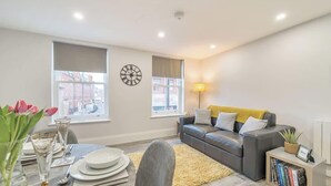 A modern living room with a sofa, a dining table set, and a lamp. - Central Windsor 1BR | Steps from Attractions (Windsor)