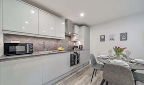 A modern kitchen with a microwave, oven, and sink. There is a dining table set with plates and glasses.