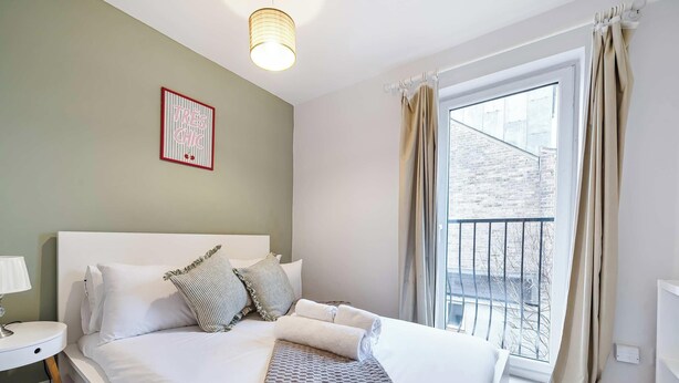 A bedroom with a bed, a bedside table with a lamp, a framed sign on the wall, and a window with curtains. - Villa Living by Lawsons (Windsor)