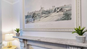 A framed historical painting of Windsor Castle on a wall, a marble fireplace, and two potted plants on a mantelpiece. - Villa Living by Lawsons (Windsor)