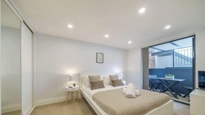 Un dormitorio moderno con una cama grande, mesitas de noche y vistas a un espacio exterior con mesa y sillas.