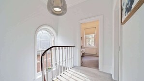 Een trap met witte balustrades en een lichtkleurig tapijt, leidend naar een kamer met een raam en een deur.