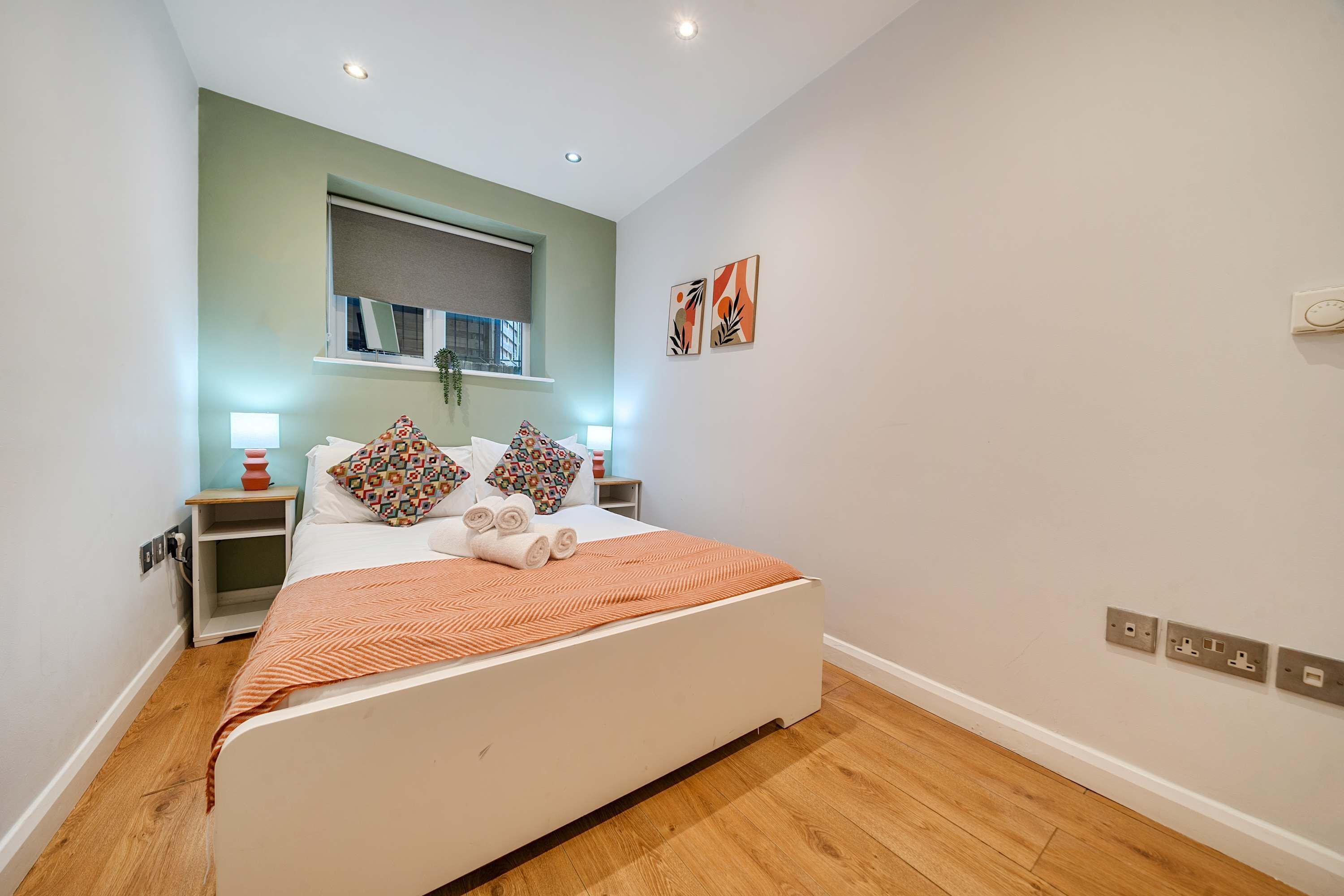 Ein Schlafzimmer mit Bett, Nachttischen, einem Fenster mit Jalousien und Bildern an der Wand.