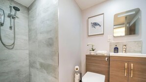 A modern bathroom with a shower, a wooden vanity, a framed artwork, and a mirror.