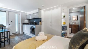 A modern hotel room with a bed, a small kitchenette, a bathroom, and a view of the outside.