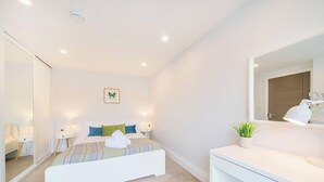 Ein modernes Schlafzimmer mit Bett, Nachttischen, einem Spiegel und einer kleinen Pflanze.